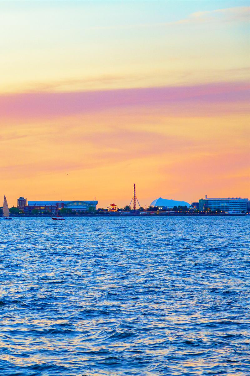 Sunset over Lake Michigan: a gold and pink sky above the Chicago lakefront, a Ferris wheel on the horizon, blue water in the foreground